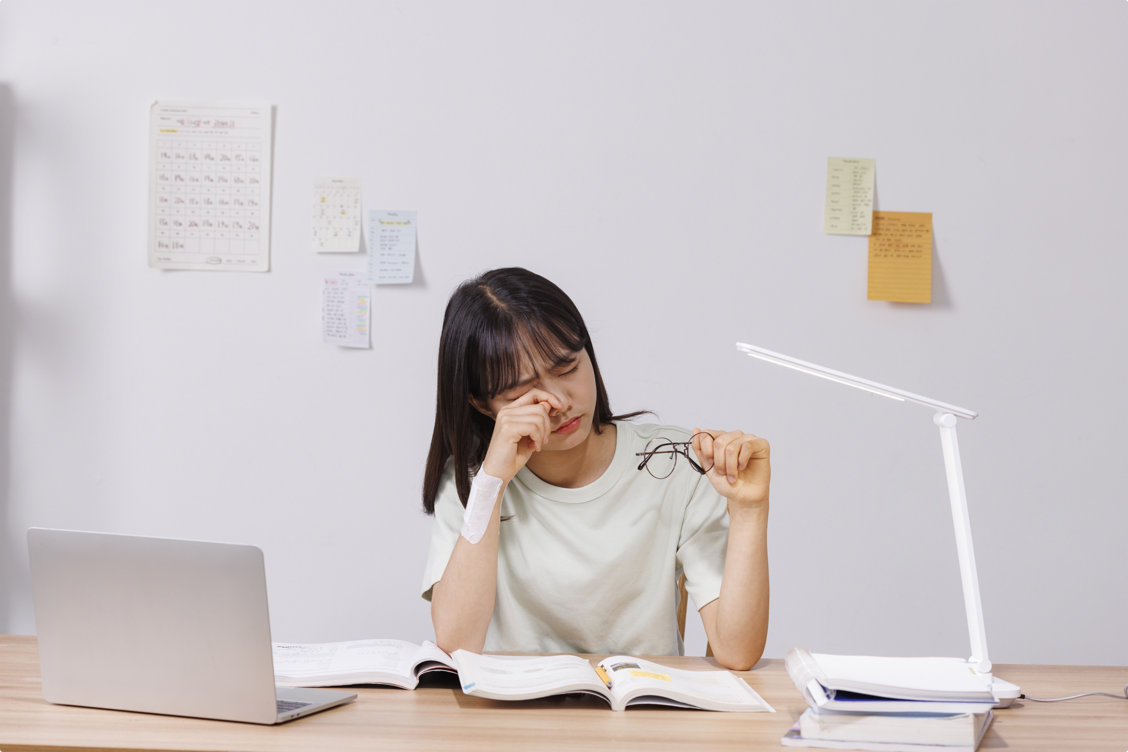 책과 노트북 앞에서 필기하는 학생
